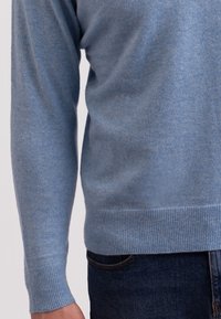 Ljusblå tröja i mjukt tyg, med rundad halsringning, ribbade muddar och ribbad nederkant. Texturerad yta med subtila variationer.