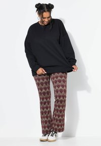 Sudadera negra de gran tamaño con hombros caídos, combinada con pantalones de campana burdeos con estampado y detalles dorados. Las zapatillas blancas completan el atuendo.
