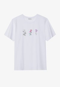 Camiseta de algodón blanca con un estampado floral que presenta tres flores ilustradas en tonos de rosa, verde y morado a lo largo del pecho.