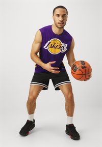 Purpurno brezrokavnik za košarko z logotipom "Los Angeles Lakers", črne kratke hlače z belimi črtami, črne teniske in oranžno košarko.