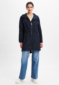 Marine waterdichte jas met verstelbare capuchon, elastische taille en rits aan de voorkant. Voorzien van twee zijzakken en lange mouwen. Lichtgewicht stof.