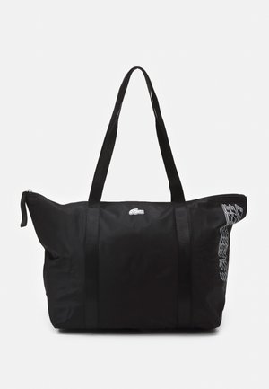 Sort nylon shopper med to skulderstropper, hvid Lacoste-logo øverst i midten og hvid grafiktekst på højre side.
