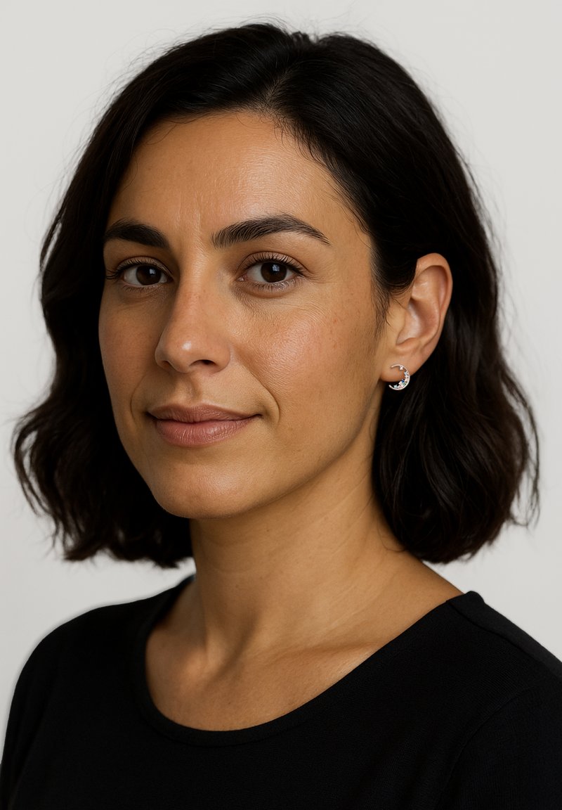 Silverskurna halvmåneformade örhängen på en kvinna med axellångt mörkt hår, klädd i en svart topp, mot en neutral bakgrund.
