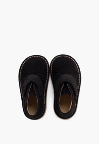 Chaussures en daim noires au design arrondi, dotées d'une sangle en velcro et de coutures beige contrastantes le long des bords et de la semelle.