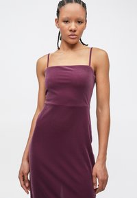 Robe sans manches bordeaux avec un corsage ajusté et un ourlet légèrement évasé. Conçue dans un tissu lisse avec de fines bretelles et un décolleté carré.