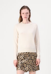 Krējuma krāsas adīts džemperis ar apaļu kakla izgriezumu un ribētu apakšu, kombinēts ar leopardu raksta svārkiem, kas rotāti ar melniem punktiem uz zelta fona.