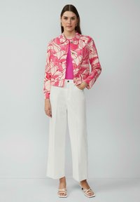 Veste courte florale rose avec boutons à l'avant, associée à un haut rose ajusté et un pantalon large blanc, portée avec des sandales blanches à lanières.