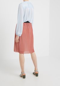 Lyseblå, plisseret bluse med lange ærmer kombineret med en koral plisseret nederdel. Højhælede sandaler med en blanding af farver og en chunky hæl.