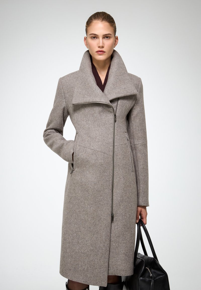 Cappotto di lana grigio con colletto alto, zip frontale completa, tasche laterali e design slanciato. Abbinato a una borsa nera.