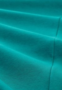 Tkanina w odcieniu zielononiebieskim z gładkim, teksturowanym wykończeniem, z delikatnymi poziomymi liniami i szwami, które tworzą warstwowy efekt.