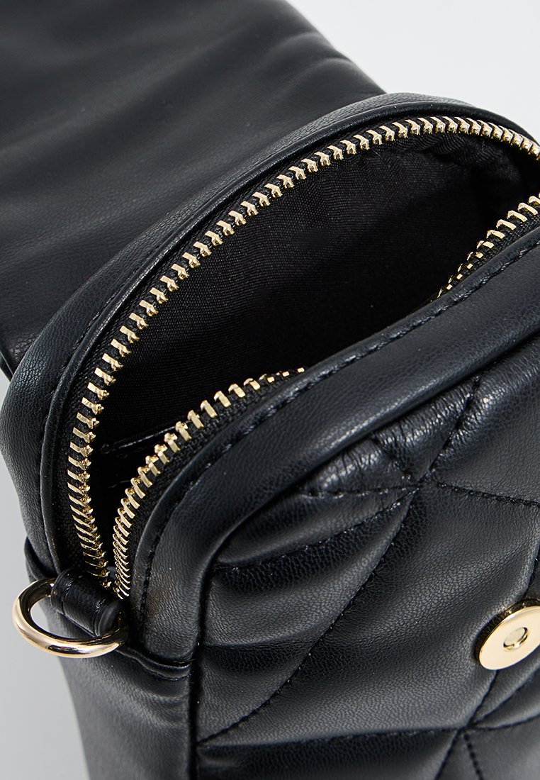 Borsa a tracolla in pelle nera con motivo trapuntato, zip e hardware dorati. Parte superiore aperta che mostra una fodera interna nera. Dettaglio anello laterale rotondo.