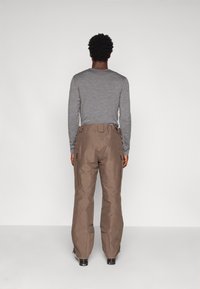 Hnedé nepremokavé nohavice s voľným strihom, bočnými zipsovými vreckami a nastaviteľnými manžetami, skombinované s dlhým šedým topom.