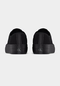 Ζευγάρι μαύρα δίχτυα sneakers χαμηλού προφίλ, που φαίνονται από πίσω, με μαύρες λαστιχένιες σόλες και γκρι λογότυπο "cK" στη φτέρνα.