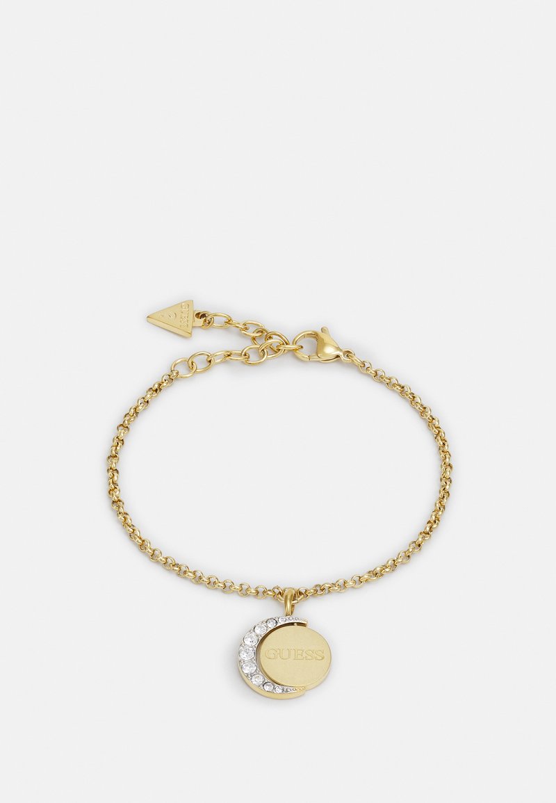 Bracelet en or avec une chaîne délicate, featuring un charme circulaire partiellement orné de cristaux transparents et gravé avec "GUESS."