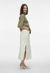 Camisa de rayas verde y blanca de manga corta combinada con una falda color crema hasta la rodilla con aberturas laterales y zapatos de tacón blancos.