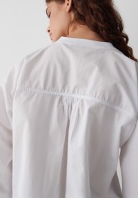 Weißes Baumwollhemd mit gerafftem Rückendetail, verfügt über eine glatte Textur und ein klassisches Hemdkragen-Design.