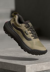 Olive green hiking sneakers with black accents, a textured rubber sole, and a durable fabric upper. Features logo and laces for secure fit.
