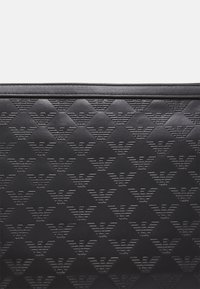 Svart läderyta präglad med ett återkommande mönster av stiliserade fågollogotyper arrangerade i diagonala rader.