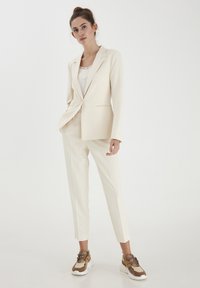 Beige skräddarsydd kavaj med en enda knapp, parat med avsmalnande matchande byxor och sneakers med neutrala toner och texturerade detaljer.