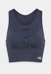 Sujeción deportiva en azul marino hecha de un tejido suave, con escote redondeado, un sutil detalle de fruncido y orificios de ventilación para mayor transpirabilidad.