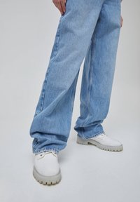 Jeans de mezclilla azul claro de pierna ancha con un ajuste holgado, combinados con zapatillas blancas que cuentan con una suela texturizada y detalles sutiles.