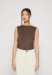Braunes ärmelloses Oberteil mit glatter Textur, kombiniert mit einem hoch taillierten, hellen Rock. Das Outfit verfügt über ein Detail mit einem einzigen Knopf.