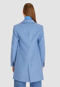 Hellblauer Wollmischungs-Mantel mit strukturierter Silhouette, Reverskragen und schwarzen Knopf-Akzenten, von hinten präsentiert.