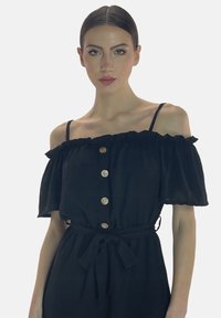 Vestido negro sin mangas con volantes en las mangas, con un cierre frontal de botones y cintura atada. Hecho de una tela ligera.