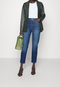 Blazer de cuero verde, camiseta blanca, vaqueros de tiro alto azules, sandalias negras con tiras y un pequeño bolso verde.