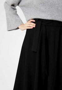 Czarna spódnica z szerokim pasem i detalem związanym, wykonana z gładkiego materiału, w połączeniu z jasnoszarym swetrem dzianinowym z rękawami dzwonami.