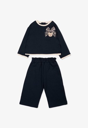 Haut noir à manches longues avec bordure beige et nœud avec détail visage de chat, associé à un pantalon large assorti avec taille élastique.