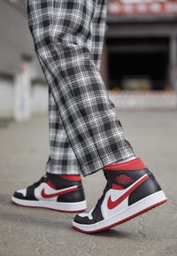 Černé, bílé a červené vysoké tenisky vyrobené z kůže a síťoviny; mají charakteristické logo s vysoce stylizovaným zakřivením a červený akcent na kotníku.