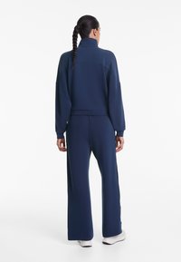 Marineblauer Trainingsanzug mit hohem Kragen, lässigem Schnitt und langen Ärmeln. Aus weichem Stoff gefertigt, mit weit geschnittenen Hosen und elegantem Design.
