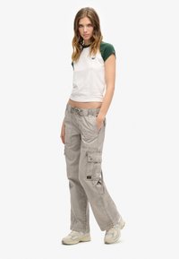 Weißes und grünes Kurzarm-T-Shirt, kombiniert mit grauen Cargo-Hosen. Die Cargo-Hosen verfügen über Taschen und einen Kordelzugbund. Tragen mit beigen Sneakers.