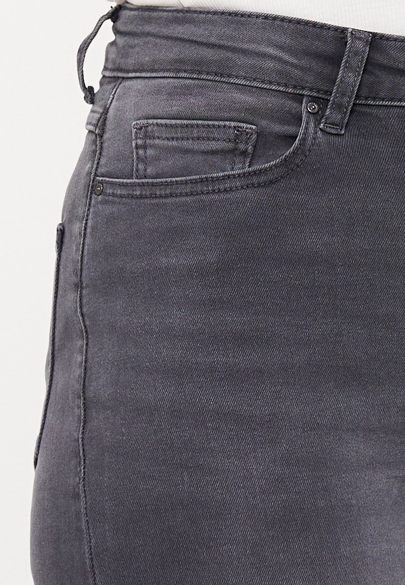 Gros plan sur un jean denim gris foncé avec passant de ceinture visible, poche avant et détails de couture de la petite poche.