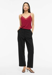 Czerwona koszulka na ramiączkach z koronkową lamówką, zestawiona z czarnymi szerokimi spodniami i czarnymi sandałkami na paski. Strój cechuje się luźnym krojem i gładką teksturą.
