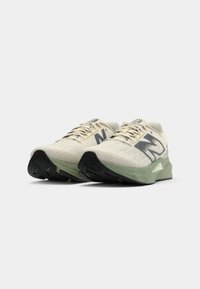 Cremefarbene Sportschuhe mit strukturiertem Obermaterial, dunkelgrünen Akzenten und einer klobigen schwarzen Sohle. Verfügt über ein Logo an der Seite und flache Schnürsenkel.