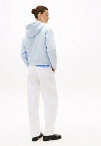 Cappuccio accorciato di colore azzurro chiaro con un cordino, abbinato a pantaloni bianchi a gamba larga. Scarpe nere completano l'outfit. Stile semplice e casual.