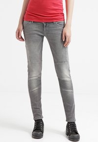 Jeans gris de corte slim con detalles acanalados en las rodillas, que cuentan con cinco bolsillos y un acabado desgastado. Combinados con botas de tobillo negras con cordones.