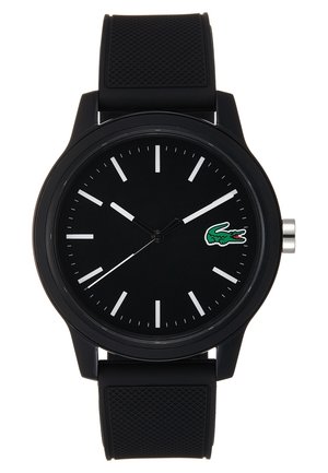 Orologio da polso analogico nero con indicatori delle ore bianchi, corona d'argento, cinturino in silicone nero texturizzato e logo di un coccodrillo verde sul quadrante.