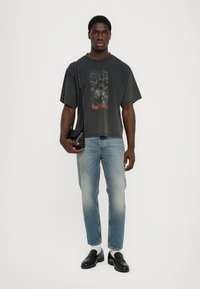 Dark gray oversized t-shirt with front graphic, light blue jeans, black leather loafers, and a small black shoulder bag.