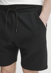 Black textured shorts featuring an elastic waist with drawstring, side pockets, and a relaxed fit.