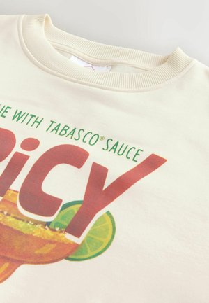 Kreemikollane ümmarguse kaelusega särk osalise tekstiga „with Tabasco® Sauce“ ja suur punane „Spicy“ margarita klaasi ja laimiviilu graafika kohal.