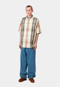Camisa de cuadros de manga corta en crema, marrón y naranja con cuello; vaqueros azul holgados; zapatos marrones de slip-on.
