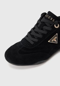 Crne visoke tenisice od antilopa sa zaobljenim vrhom, toniranim vezicama i zlatnim detaljima logotipa sa strane i na jeziku. Teksturirani detalji na gornjem dijelu.