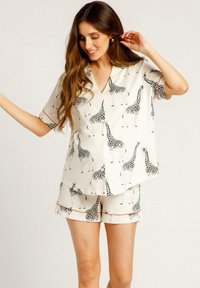 Ensemble de pyjama à manches courtes avec un imprimé girafe sur fond crème. Comprend une chemise à col avec bordure rouge et un short assorti.
