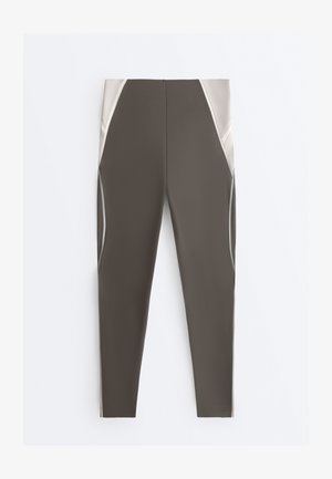 Vysoký pás legíny v olivovo zelenej a béžovej farbe s panelovým dizajnom a švovými líniami, navrhnuté pre športové oblečenie.