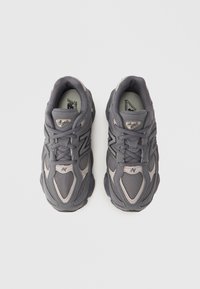 Gray athletic shoes with mesh and synthetic materials, featuring a textured design, curved shape, and a subtle "N" logo on the side.