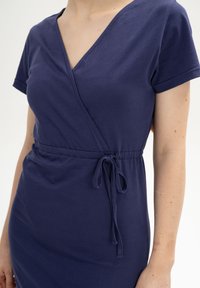 Marineblaue Wickelkleid mit kurzen Ärmeln, aus weichem Stoff. Verfügt über eine gebundene Taillendetail und ein V-Ausschnitt-Design. Einfach und unaufgeregt.