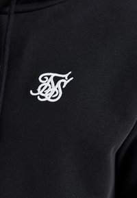 Black hoodie featuring a textured fabric, with a white embroidered logo on the chest. Close-up view focusing on material and design details.